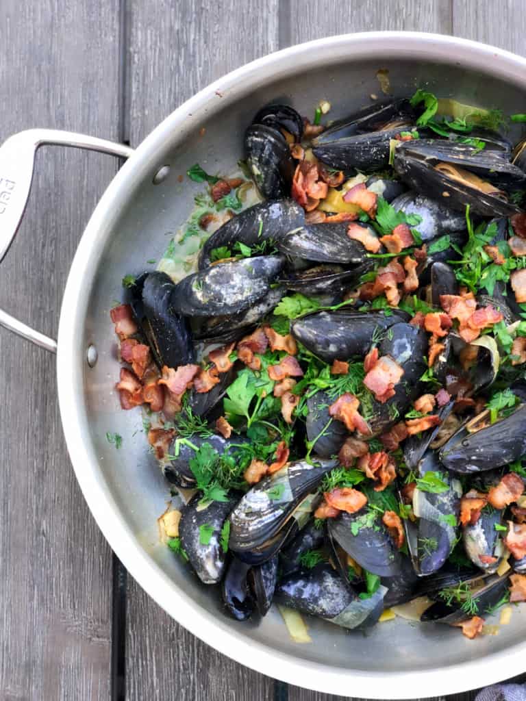 steamed mussels with leeks and bacon in pan
