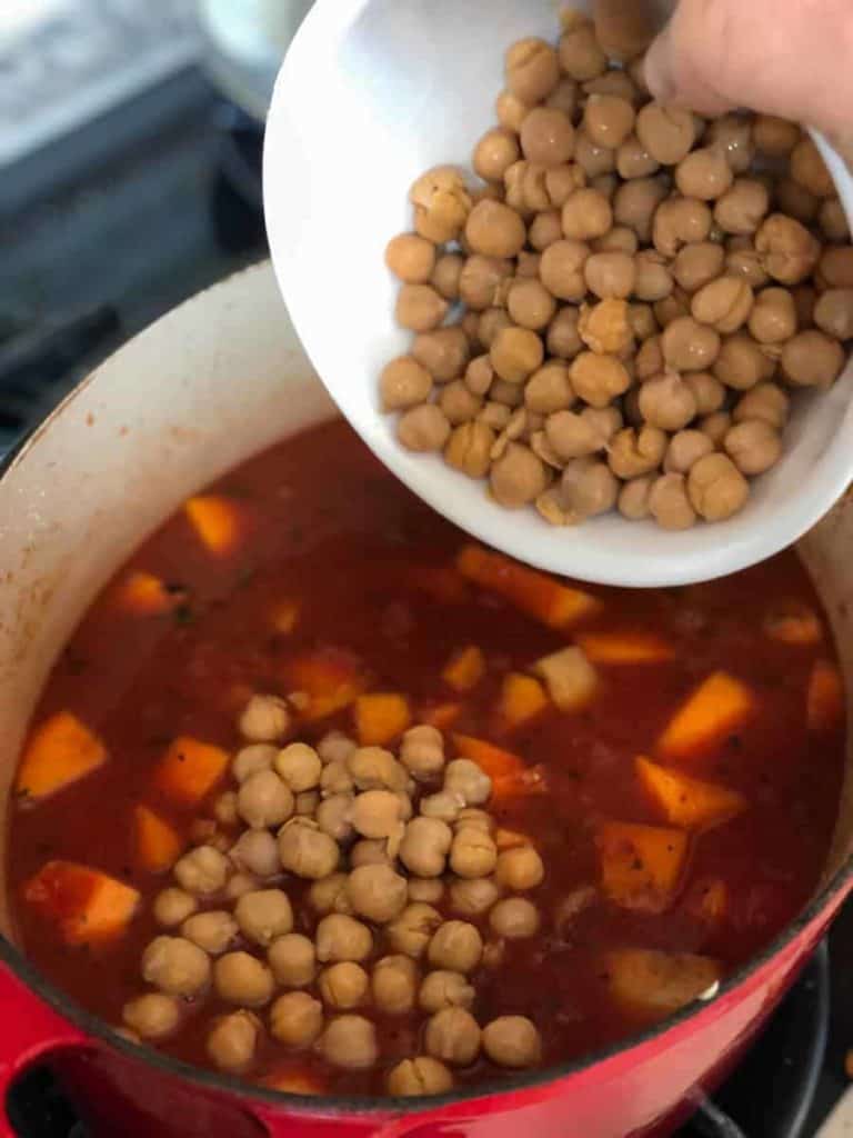 adding chickpeas to a pot with sauce