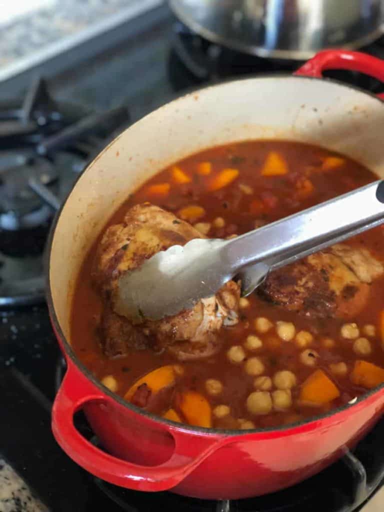 Adding chicken with prongs to a pot with sauce