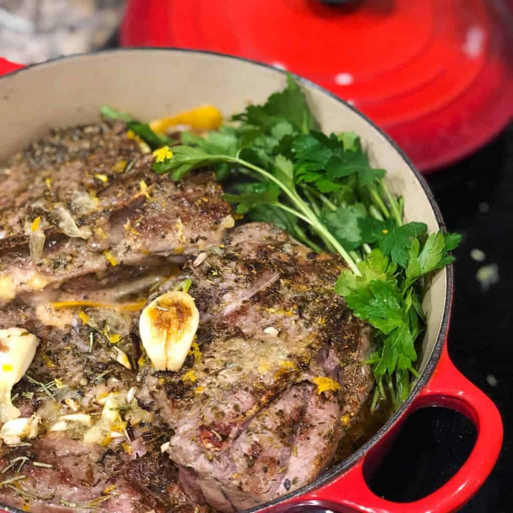red dutch oven with braised lamb in liquid