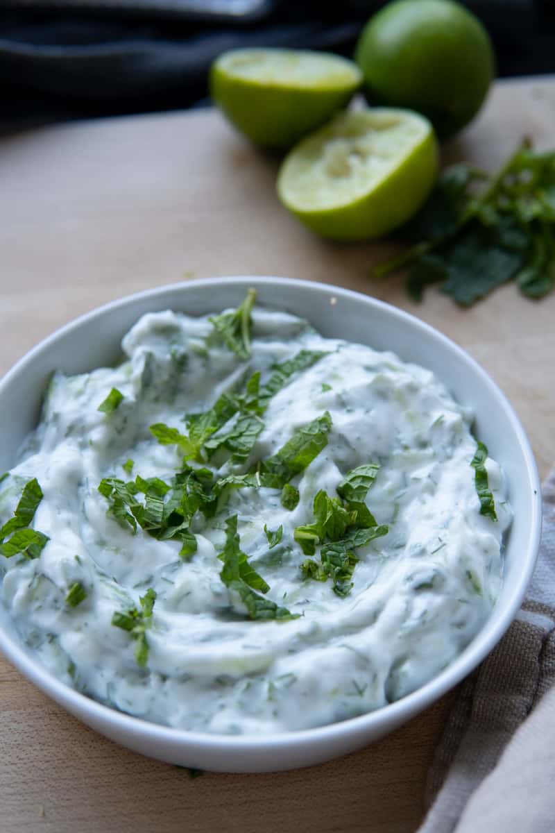 tzatziki yogurt sauce in bowl with mint garnish and limes on side