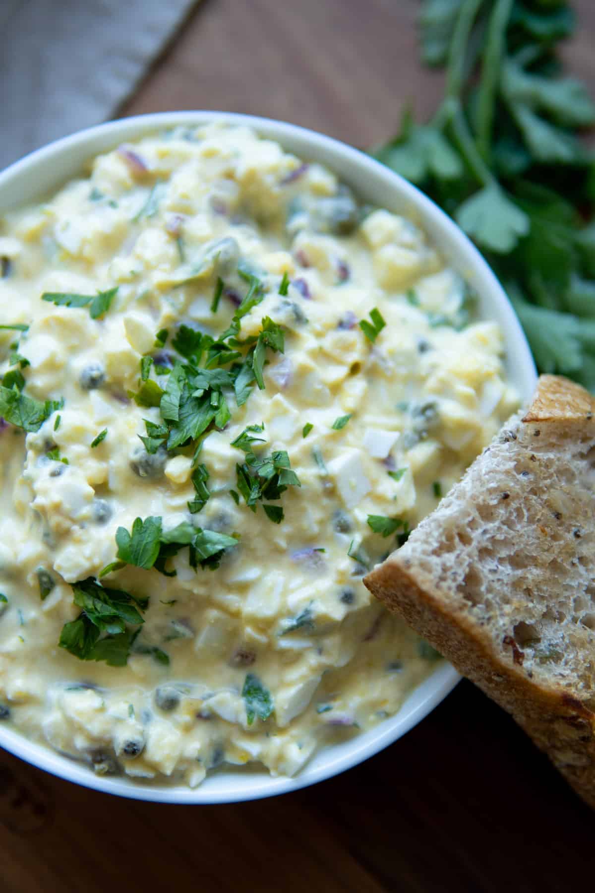 No mayo egg salad in a bowl topped with chopped herbs and a piece of toast.