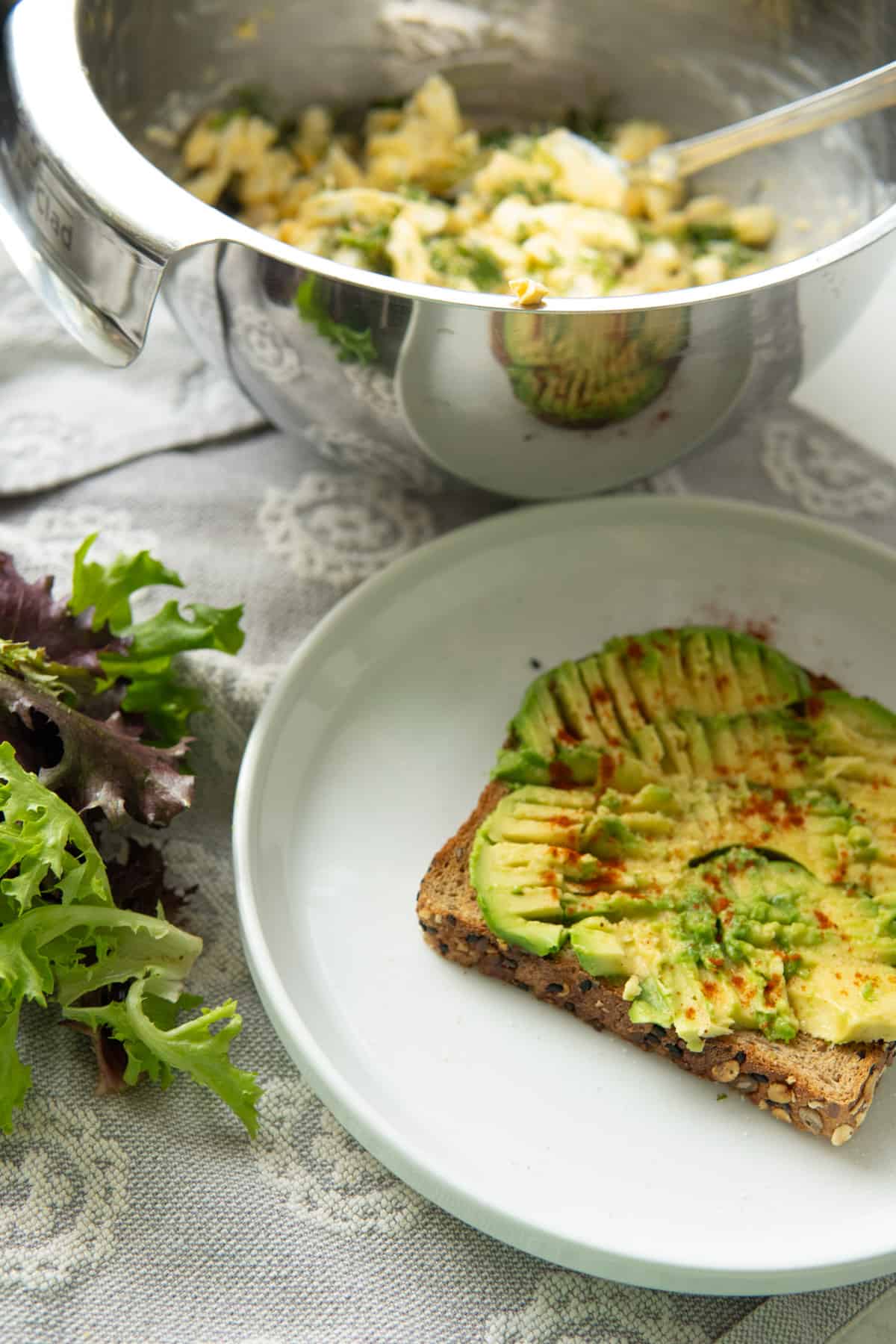 toast with avocado on a plate, sprinkled with paprika and a bowl of egg salad on side 