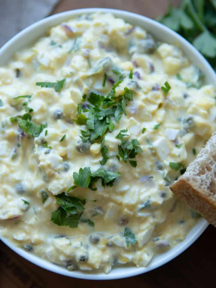 No mayo egg salad in a bowl topped with chopped herbs and bread.