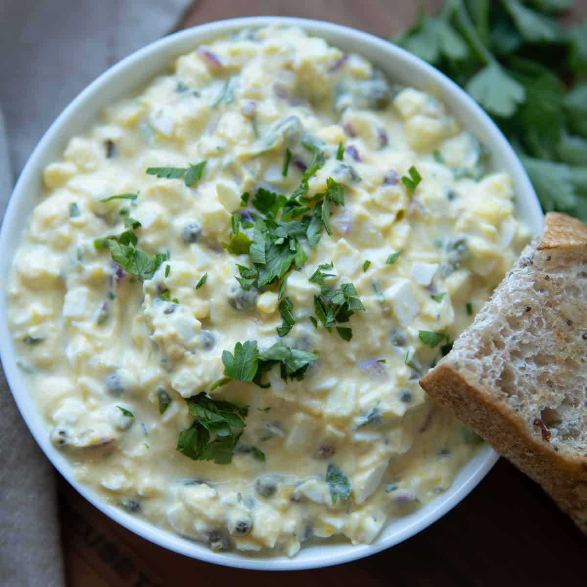 No mayo egg salad in a bowl topped with chopped herbs and bread.