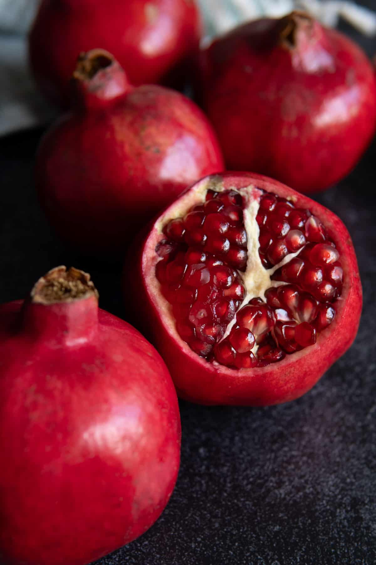 Three whole pomegranates next to one cut open.