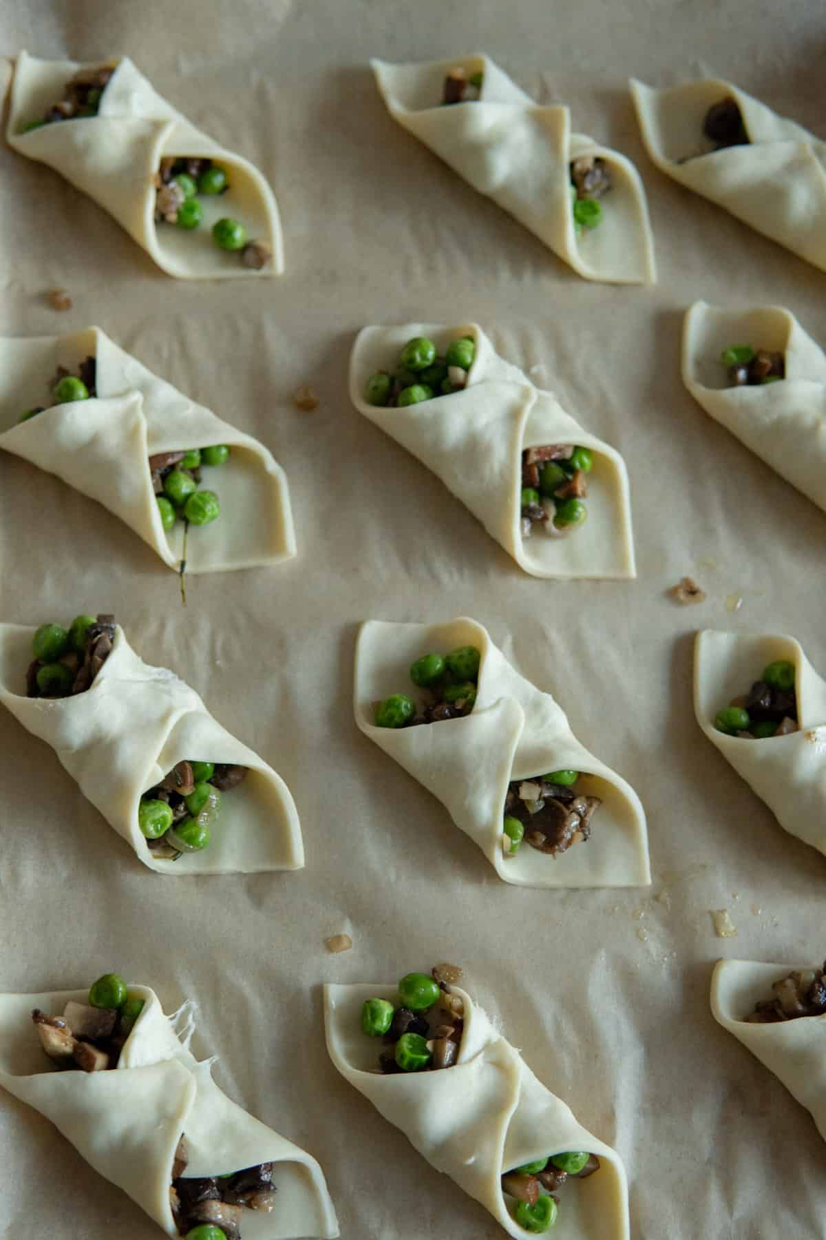 Folded mushroom puff pastries on a baking sheet before baking.