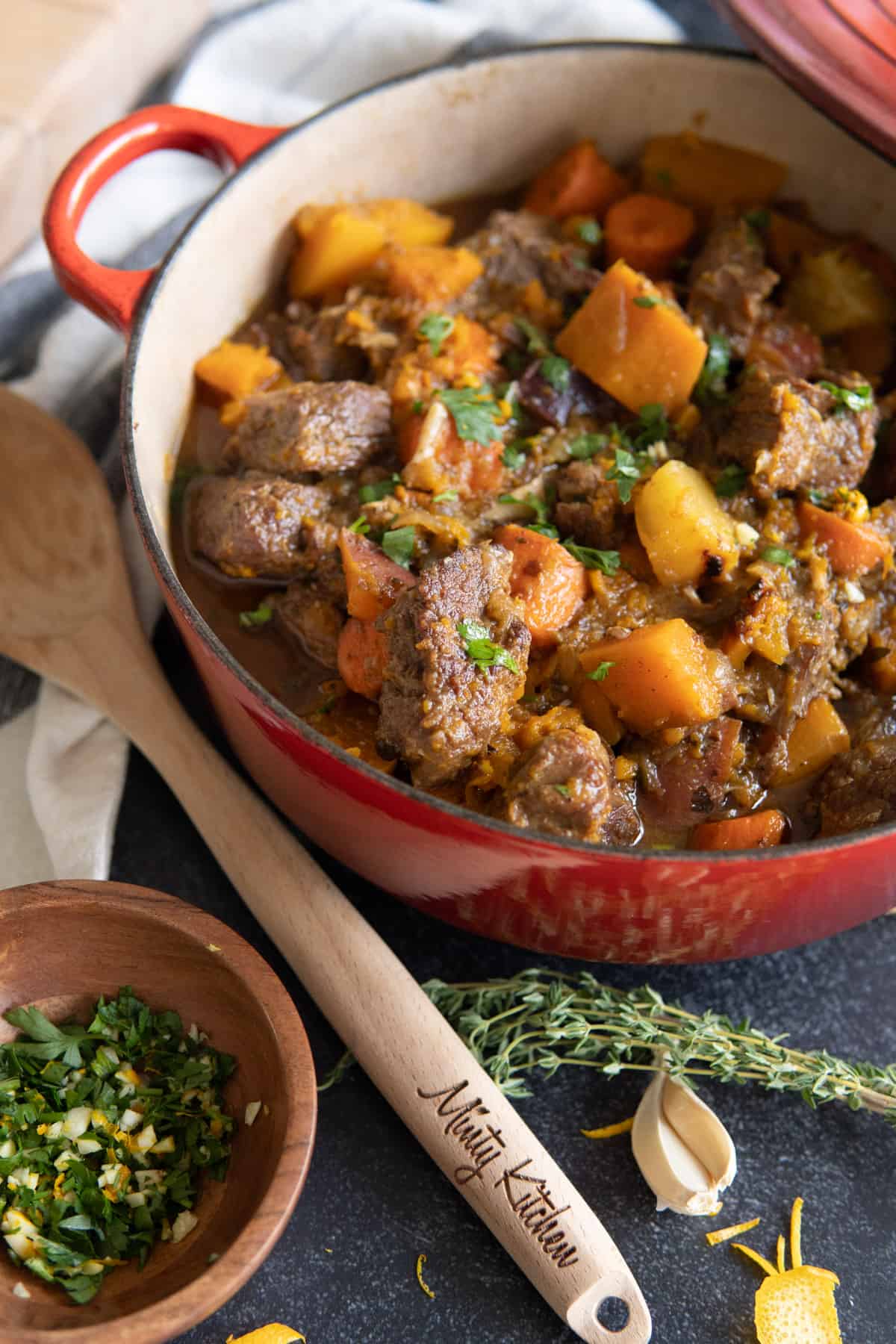 Beef stew in a pot with parsley and orange gremolata in a small bowl.
