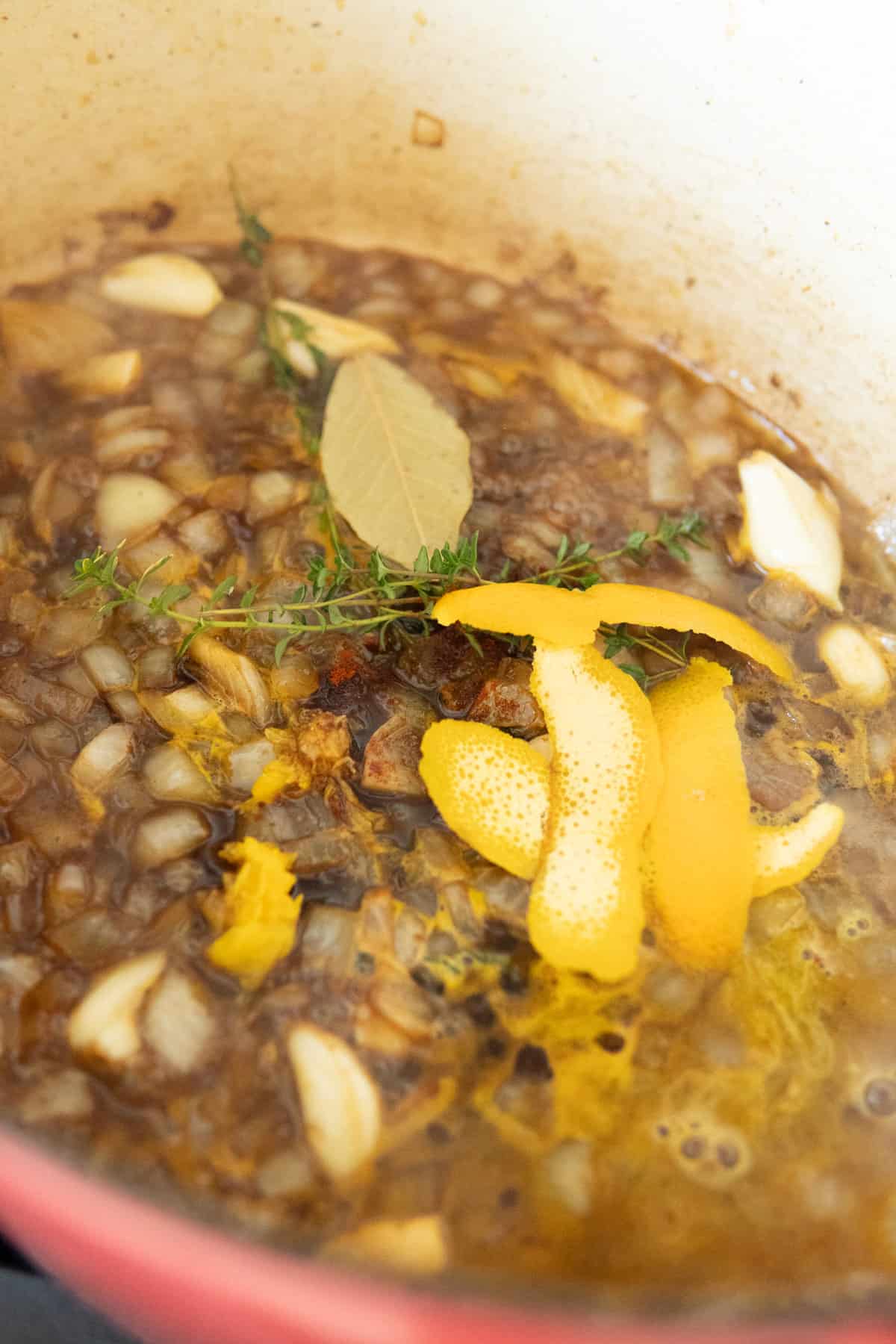 Beef stock with onions, seasonings, thyme and orange peels simmering in a pot.