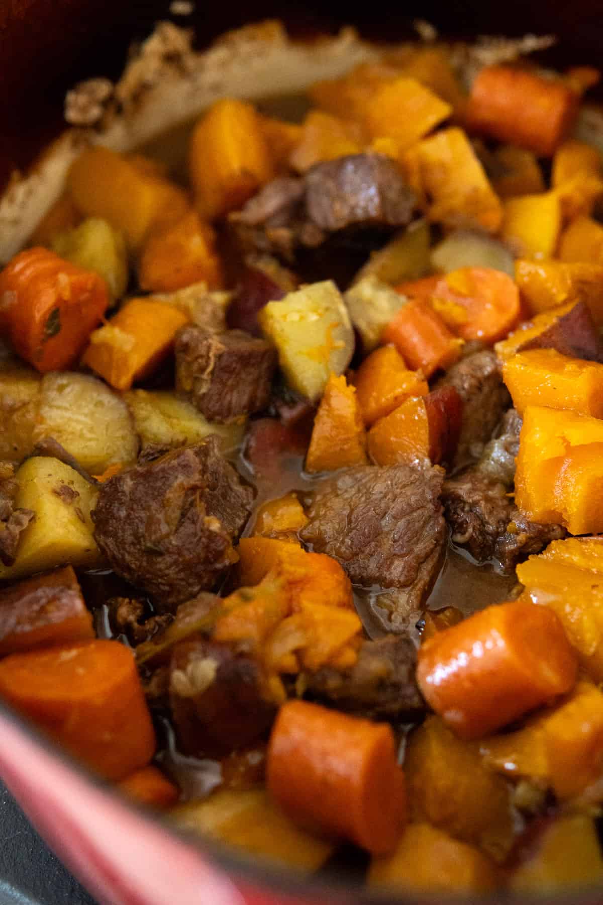 Cooked beef stew in a pot with carrots, potatoes, and butternut squash.