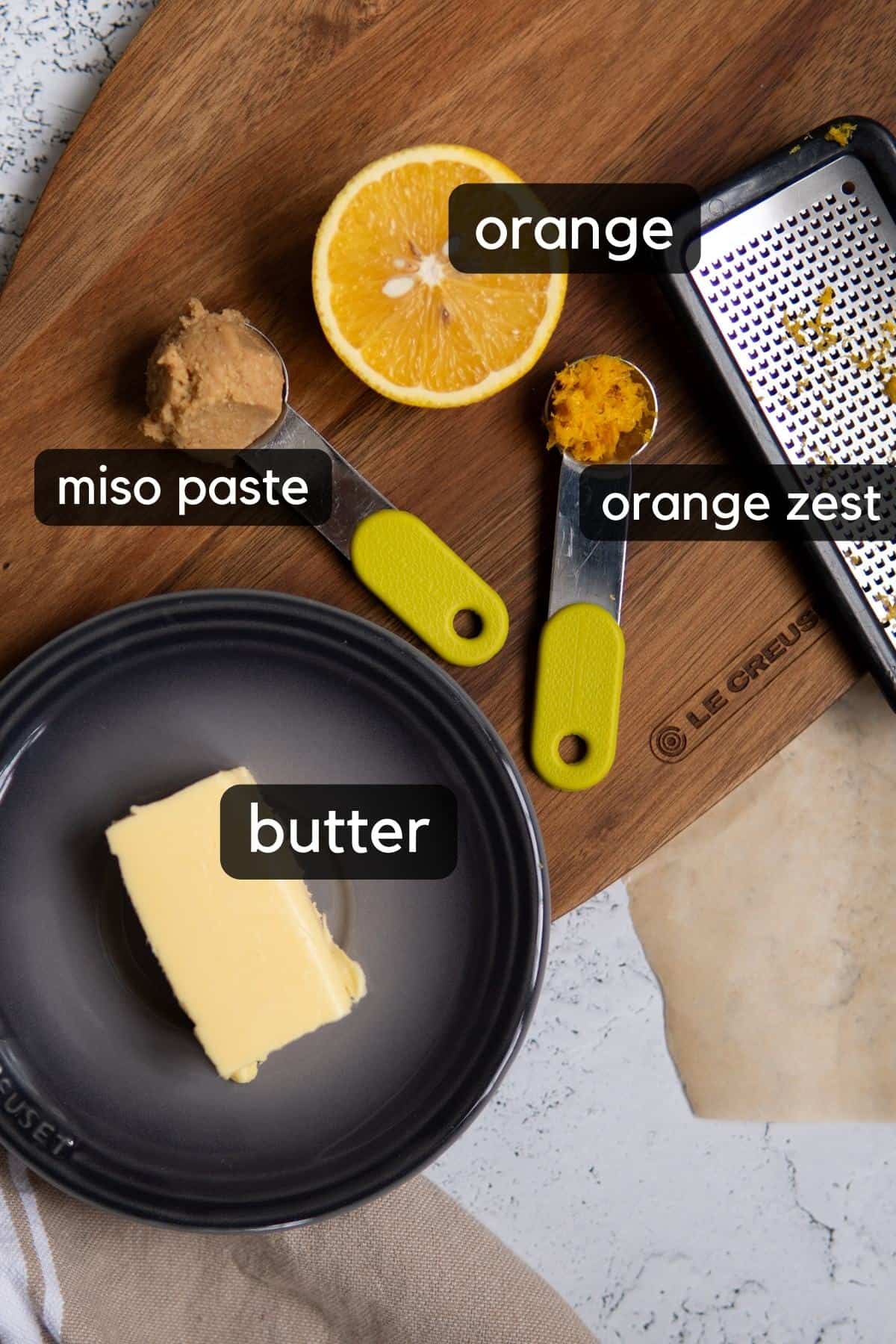plate with butter, measuring spoons with miso paste, orange zest and half an orange. 
