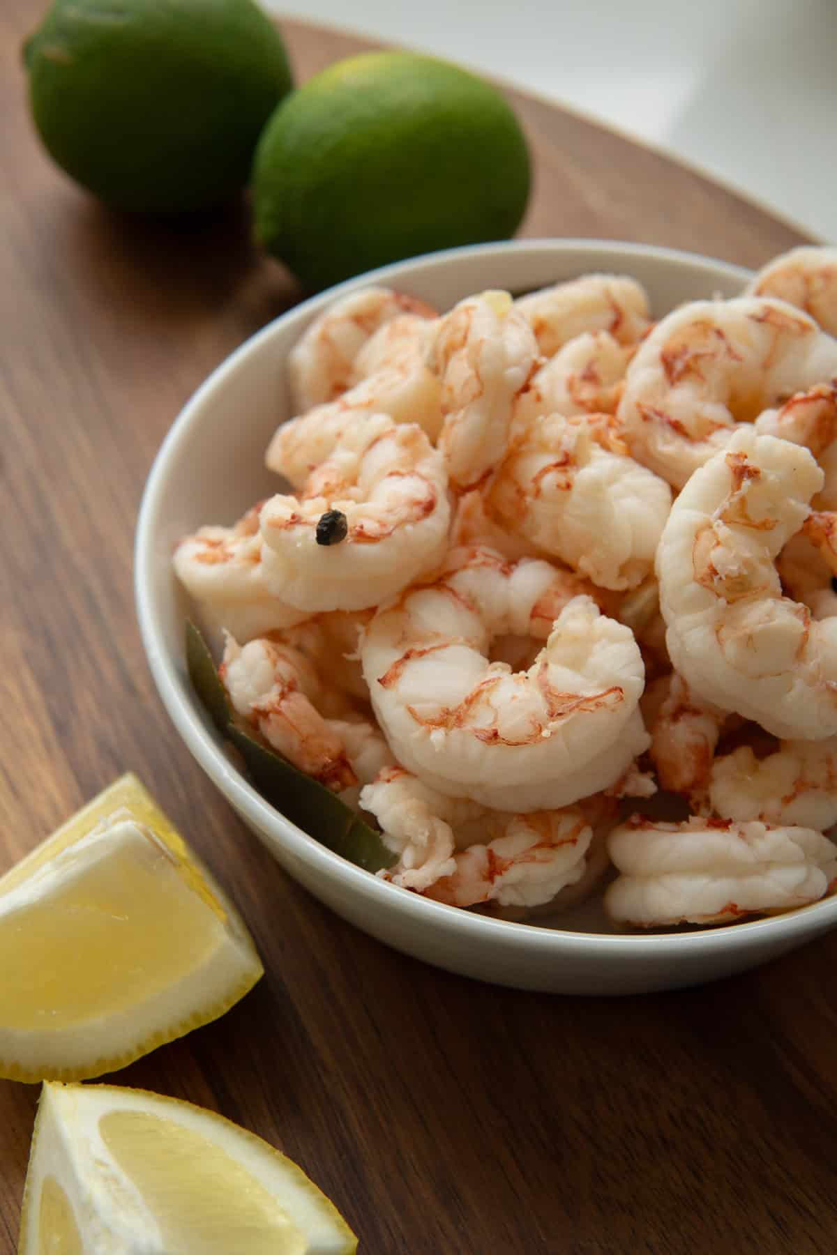 wooden board with limes,  lemon wedges and a small bowl of boiled shrimp