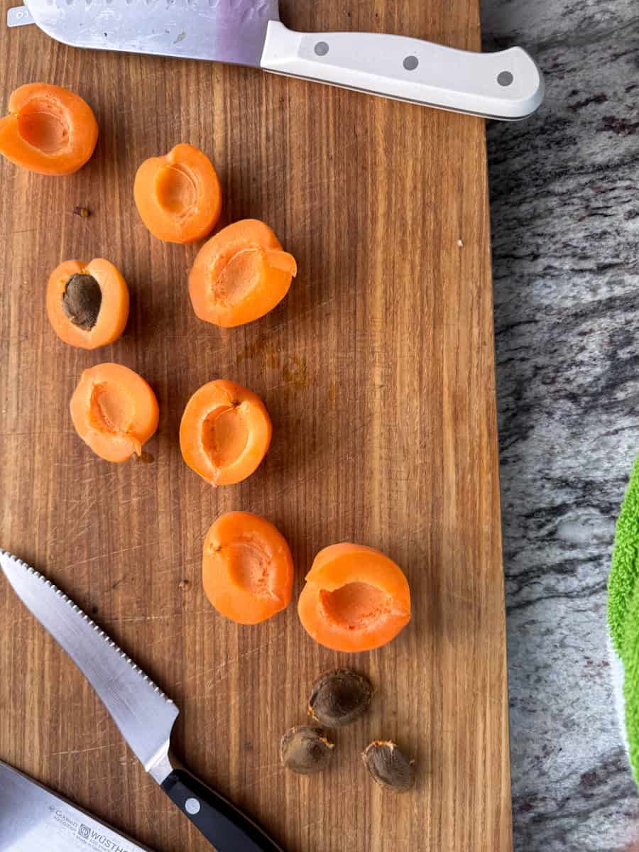 cutting board with apricots cut in half and pits next to them. 