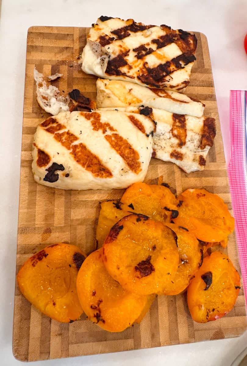 grilled halloumi pieces and grilled apricot halves on a cutting board. 