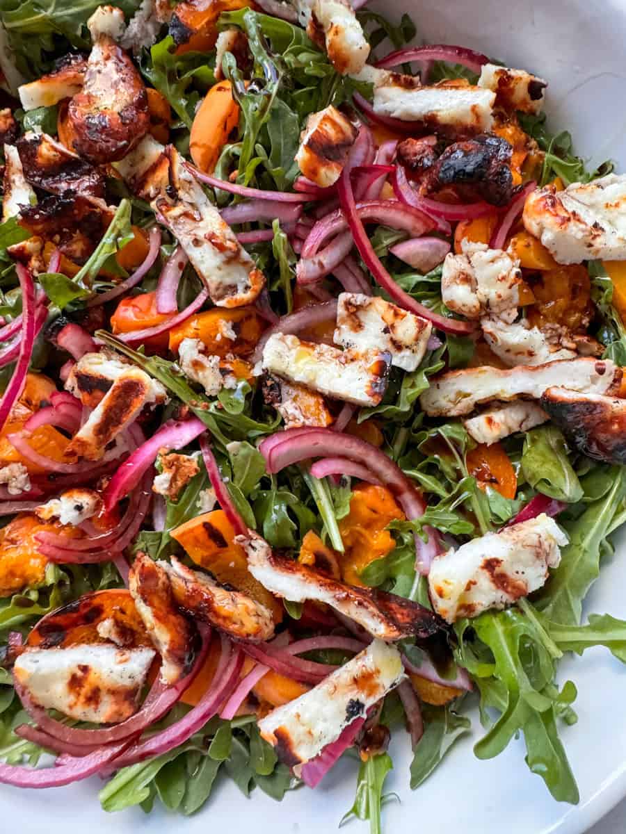 close up of arugula salad with grilled halloumi, apricots, and red onion 