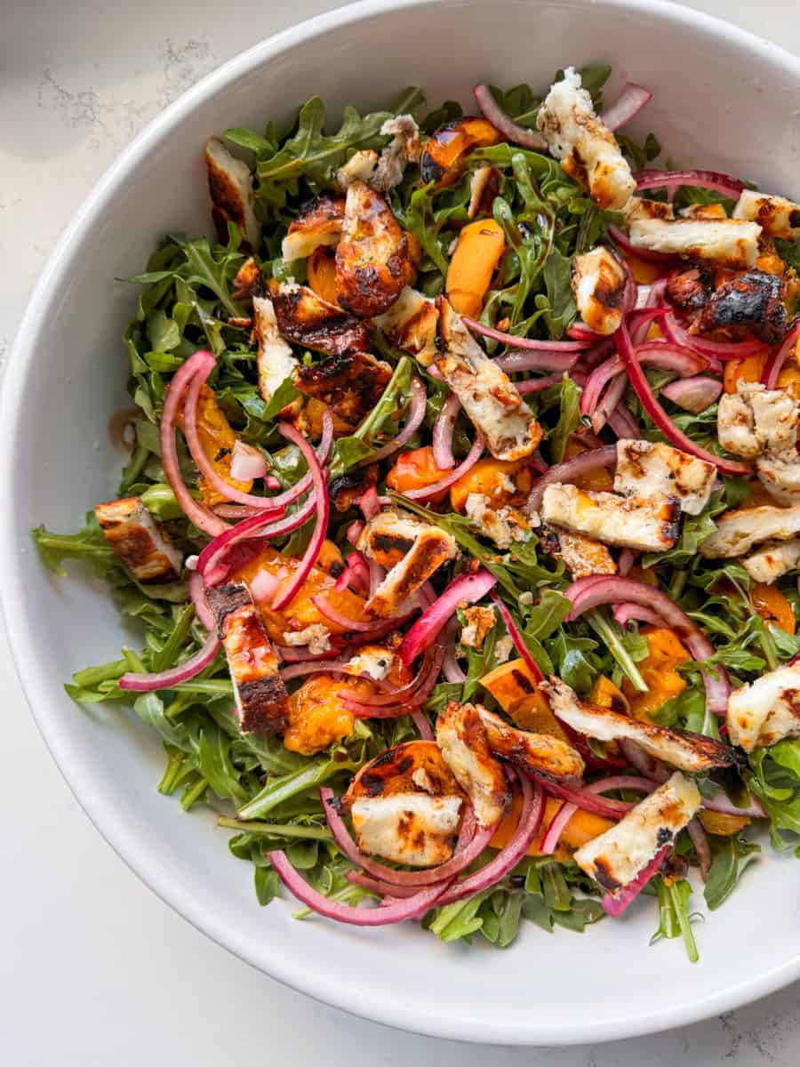 large white bowl with arugula, grilled peaches and halloumi, red onion. drizzled with balsamic. 