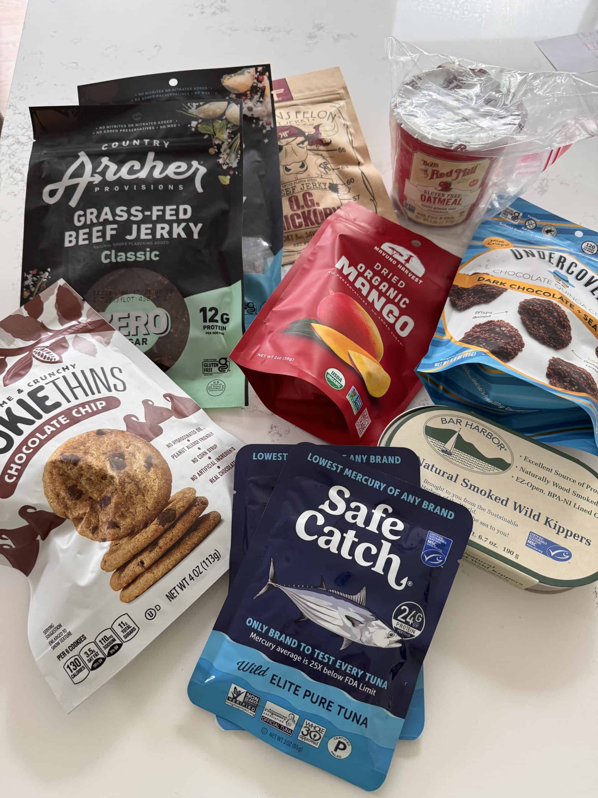 an assortment of packaged travel snacks like tuna and jerky on a kitchen table 