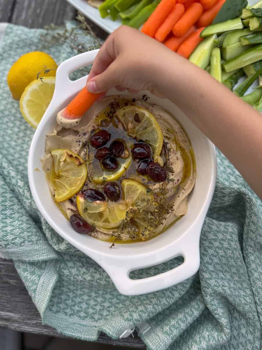 childs hand dipping carrot into hummus 