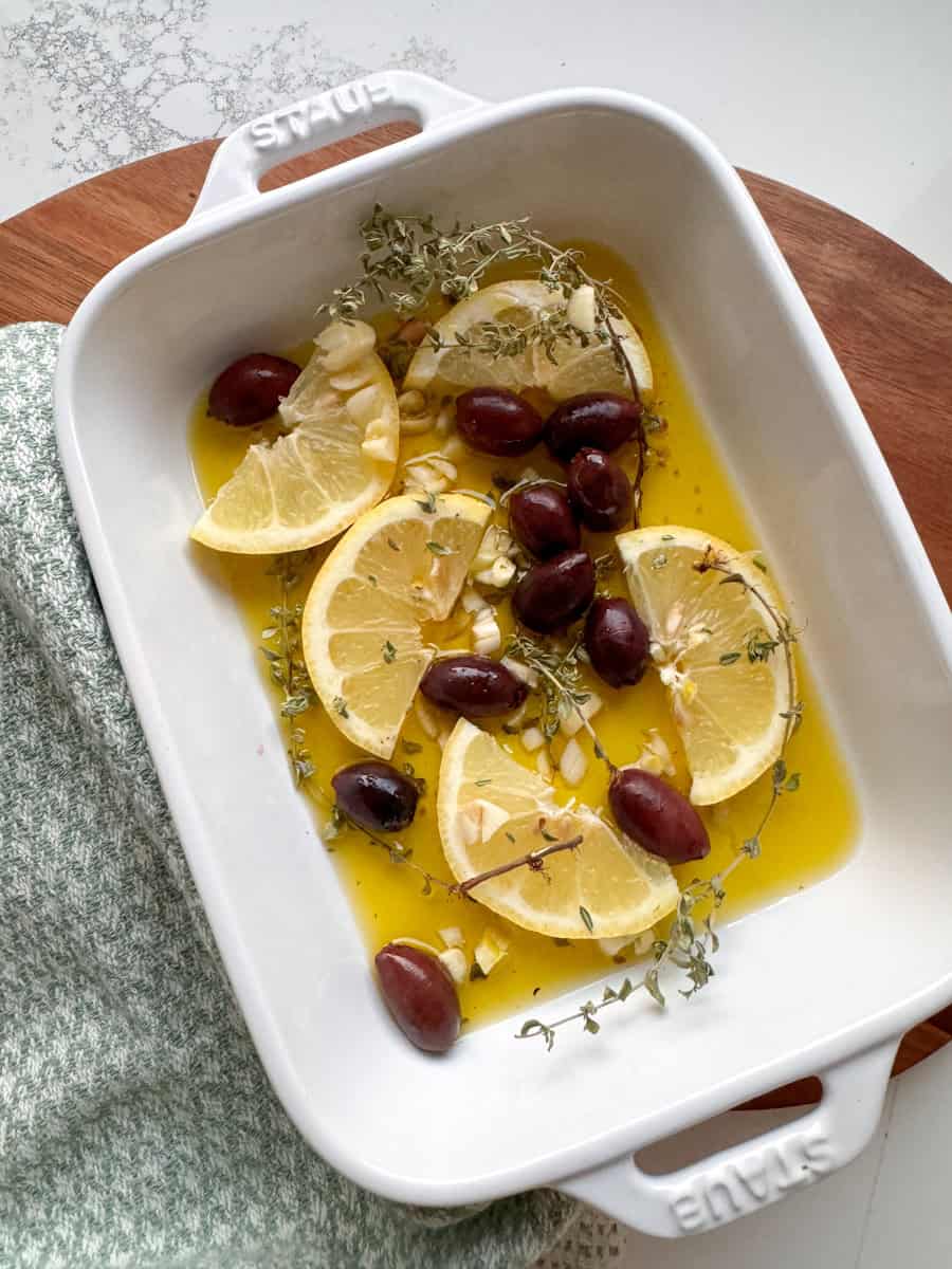 white ceramic dish with olive oil, lemon slices, olives, garlic, and thyme