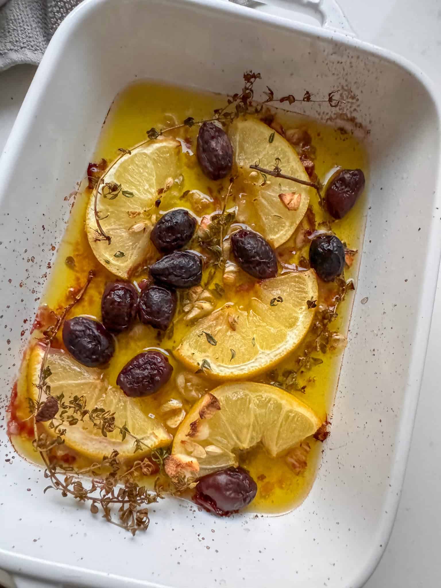 dish with roasted olive oil, lemons slices, olives and thyme