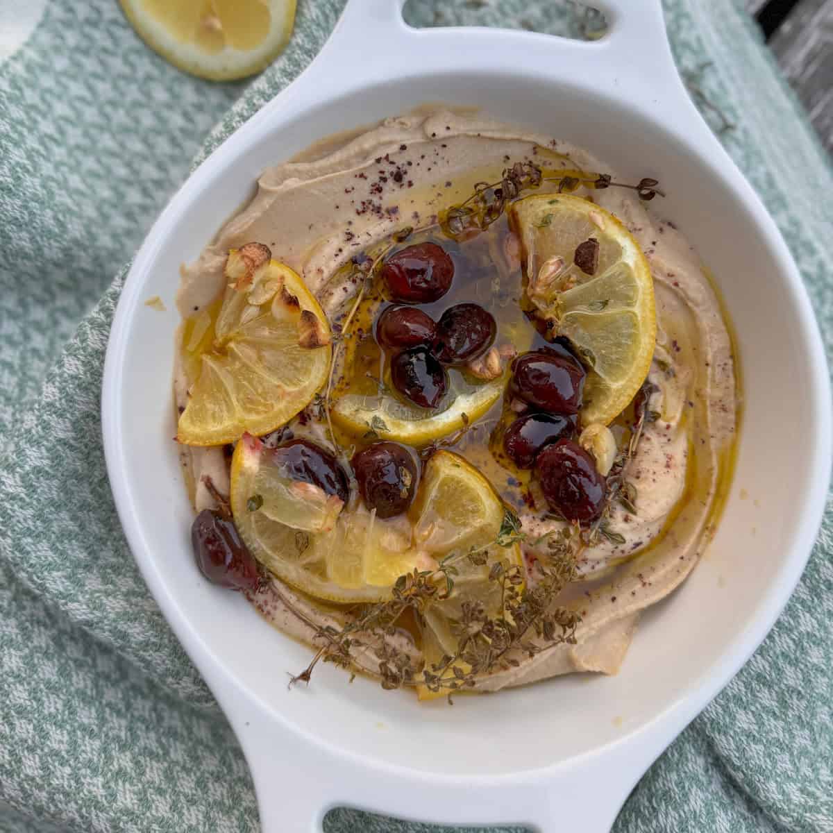 white bowl with hummus, olive oil, and roasted lemons and olives 