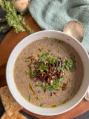 bowl of creamy mushroom soup with spoon next to it, and 2 slices of bread, fresh herbs