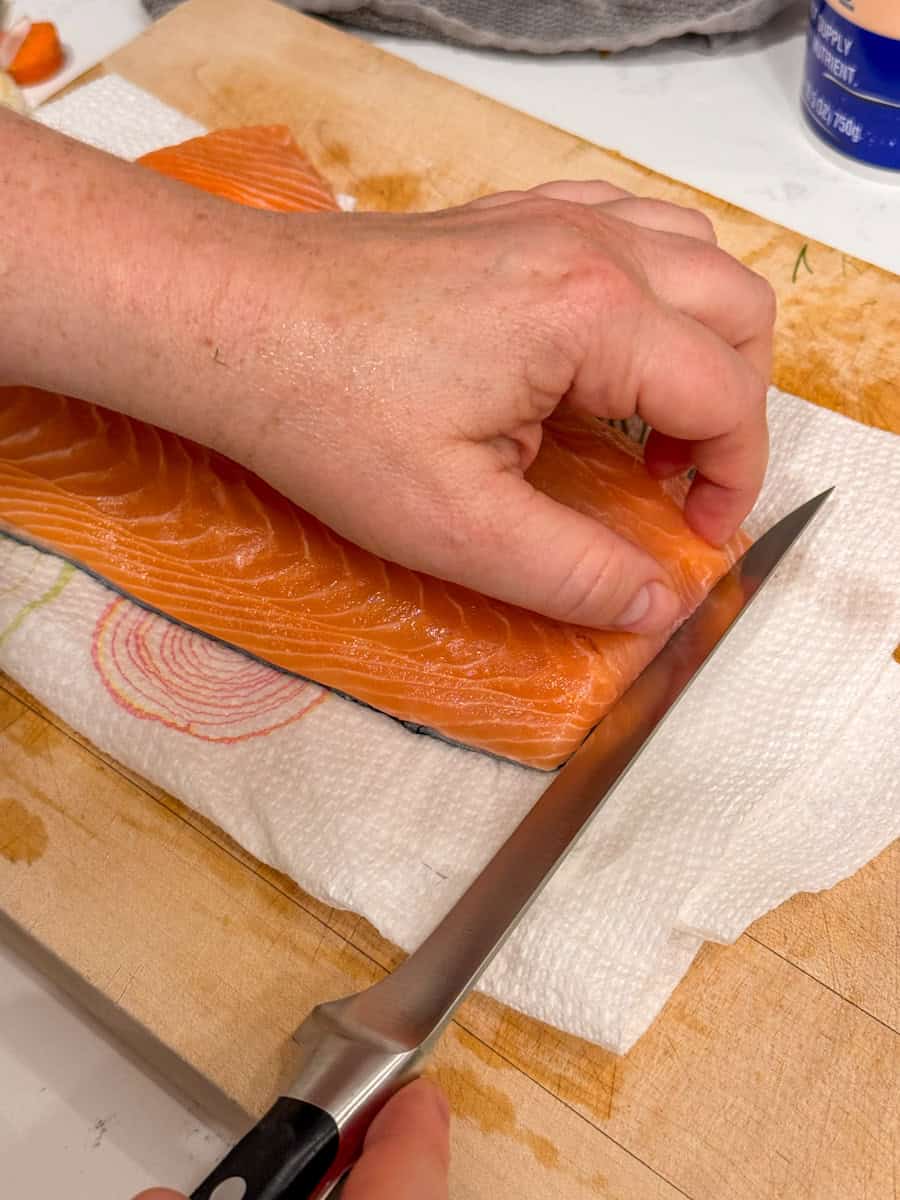 salmon with skin on on a cutting board with hand and a knife