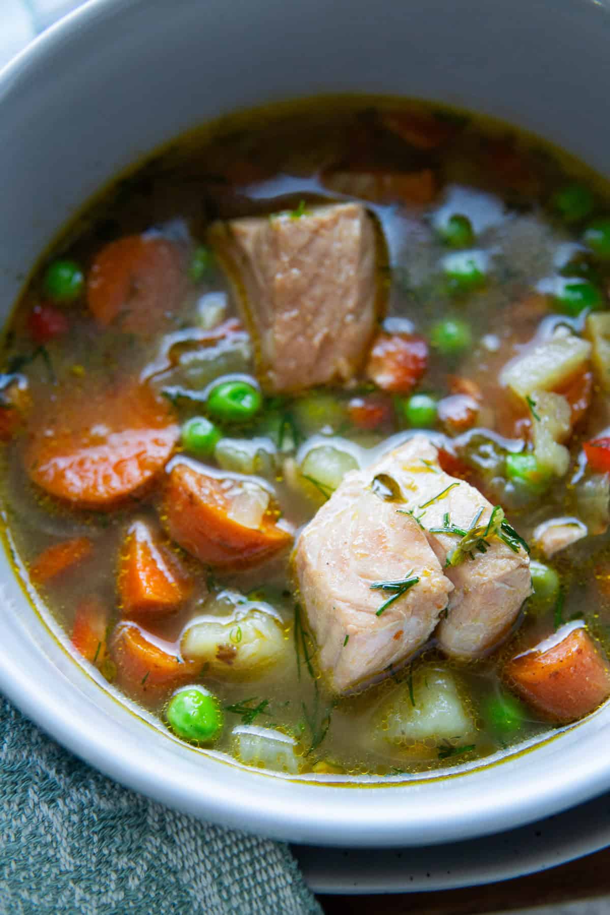 close up of a bowl with fish soup, carrots, peas, salmon 