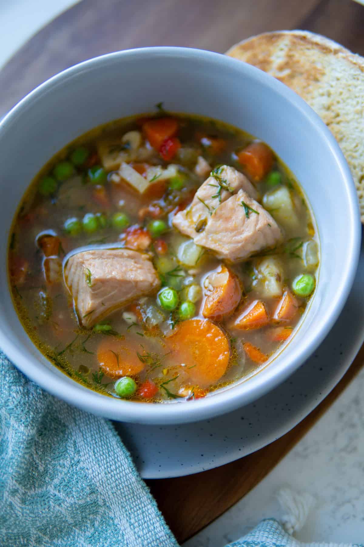 a bowl with fish soup and a side of bread on a plate. 