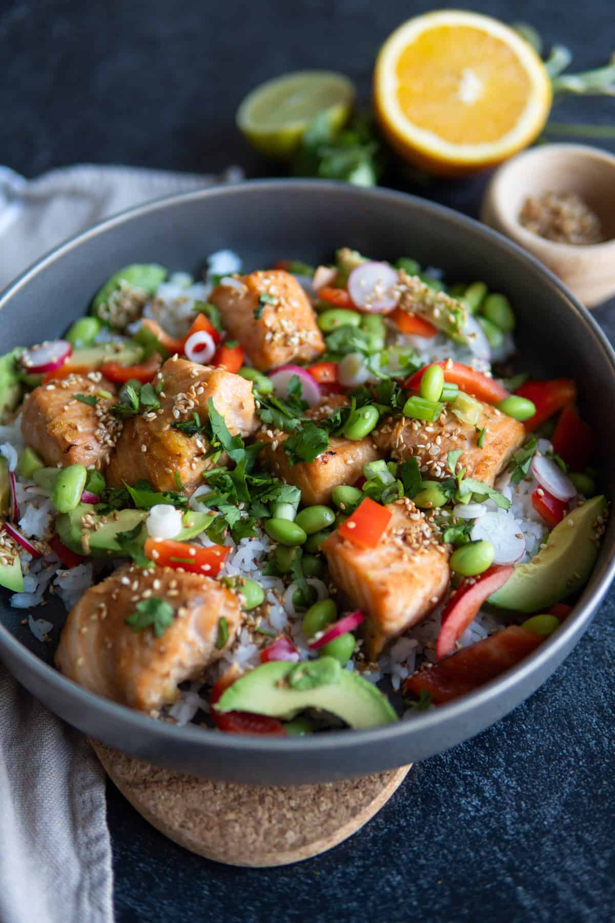 large bowl with salmon chunks, sesame seeds, white rice, edamame, peppers, avocado