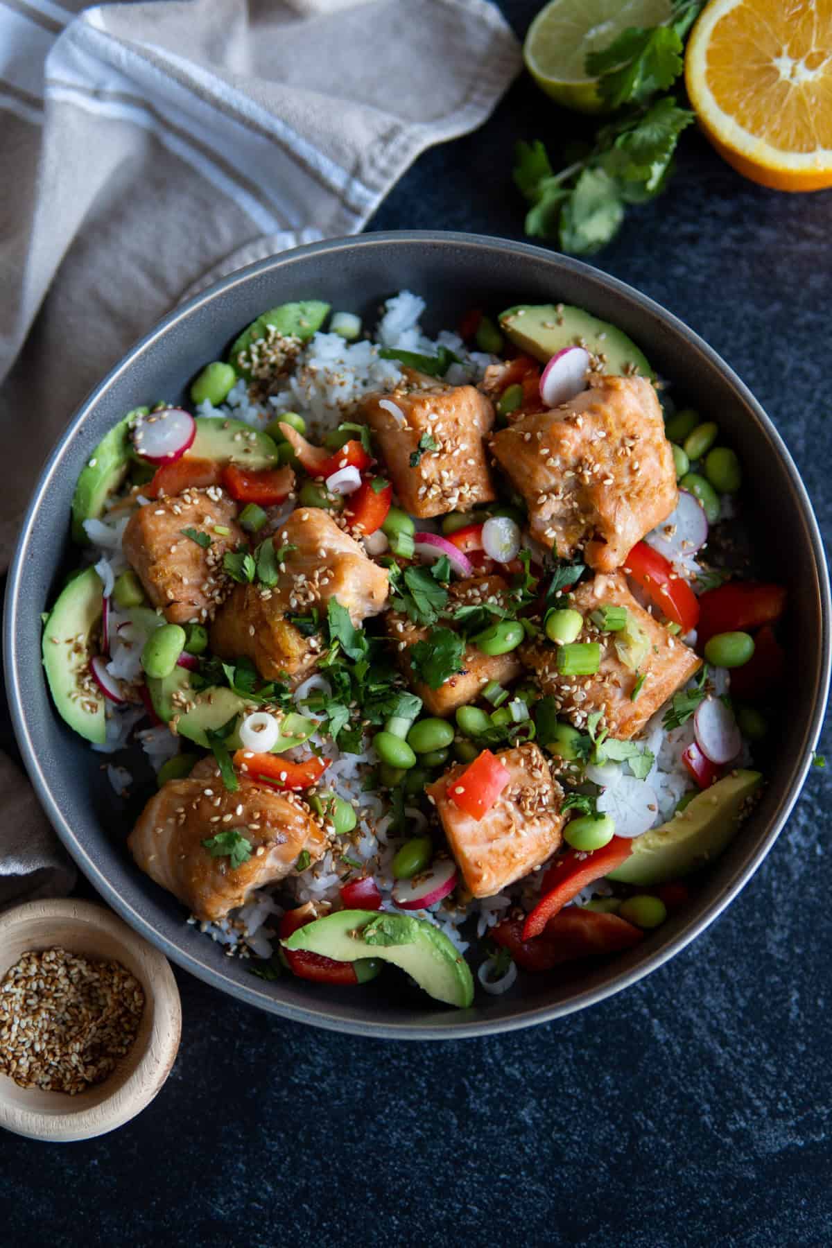 a finished bowl ready to serve with rice, veggies and salmon pieces. garnished with sesame seeds. 