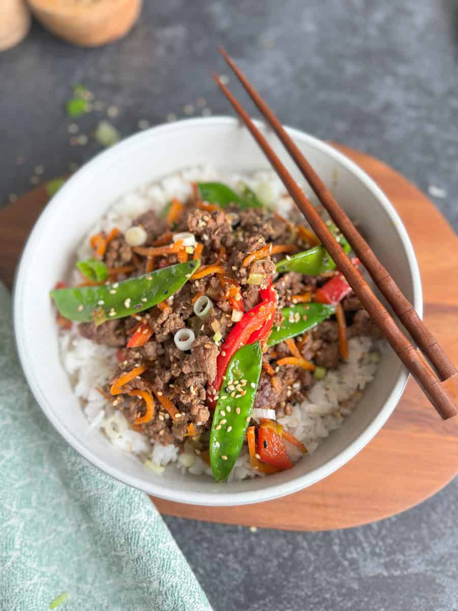 bowl with rice and stir fry with vegetables and chop sticks on top of bowl. 