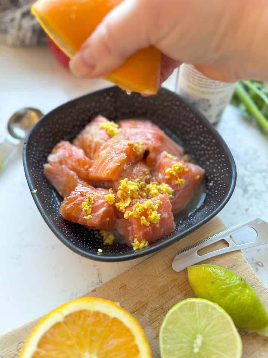 bowl of raw salmon pieces with grated ginger on top and a hand squeezing orange juice 