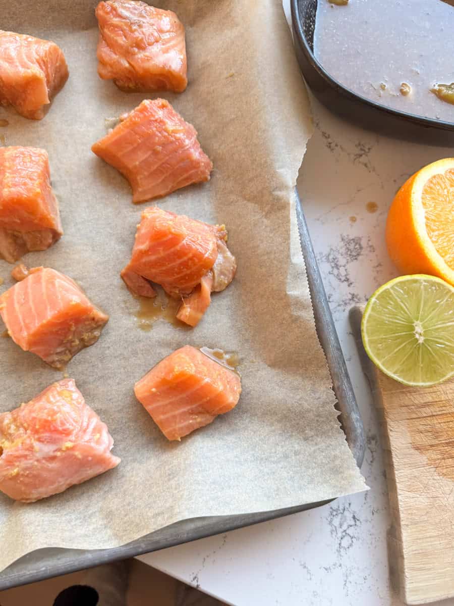 a baking sheet with parchment paper and marinated salmon chunks spread out equally