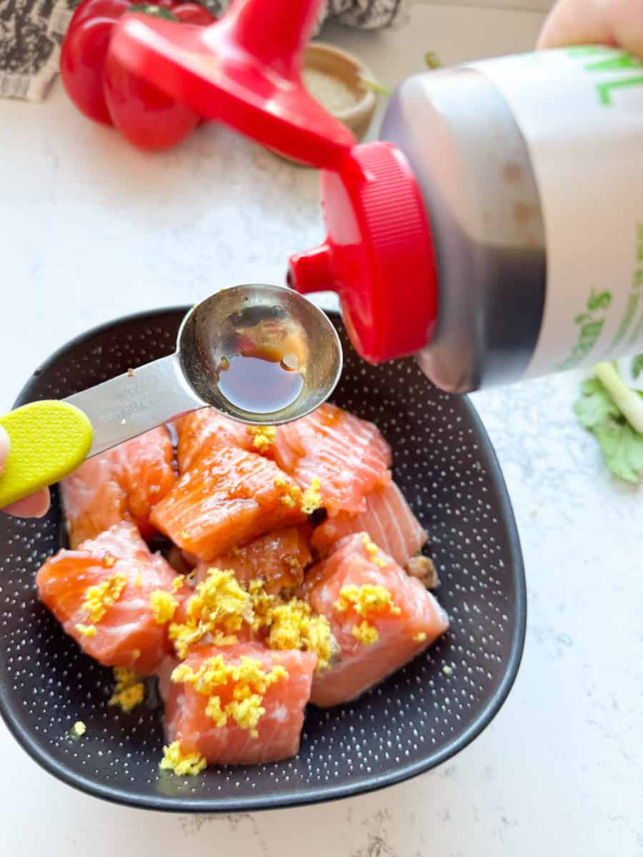 black bowl with salmon pieces, grated ginger and a spoonful of sauce being poured 