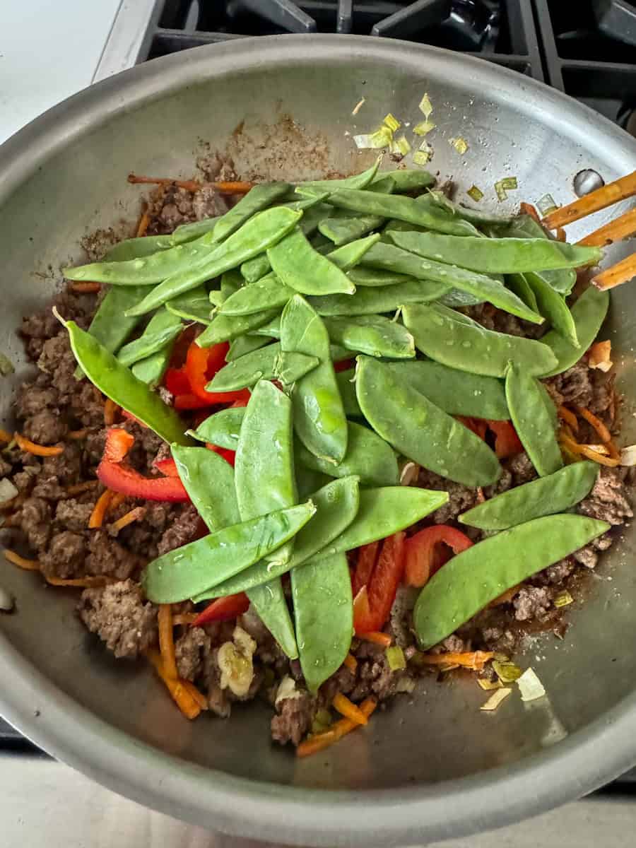 large stainless steel pan with meat and snow peas on top