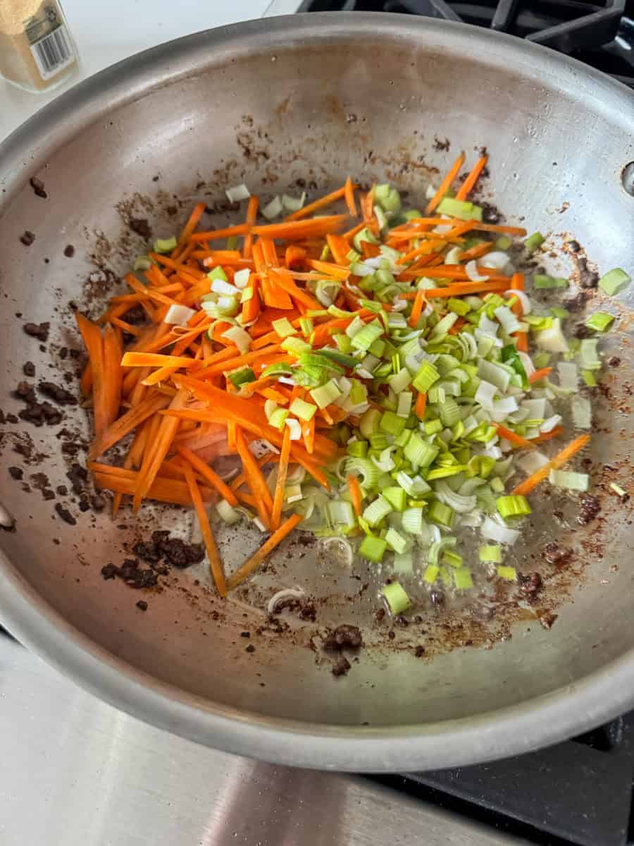 carrots and leeks sautéing in a pan. 