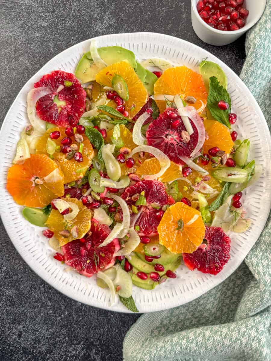 round white plate arranged with oranges, fennel, avocado, mint and pomegranates. 