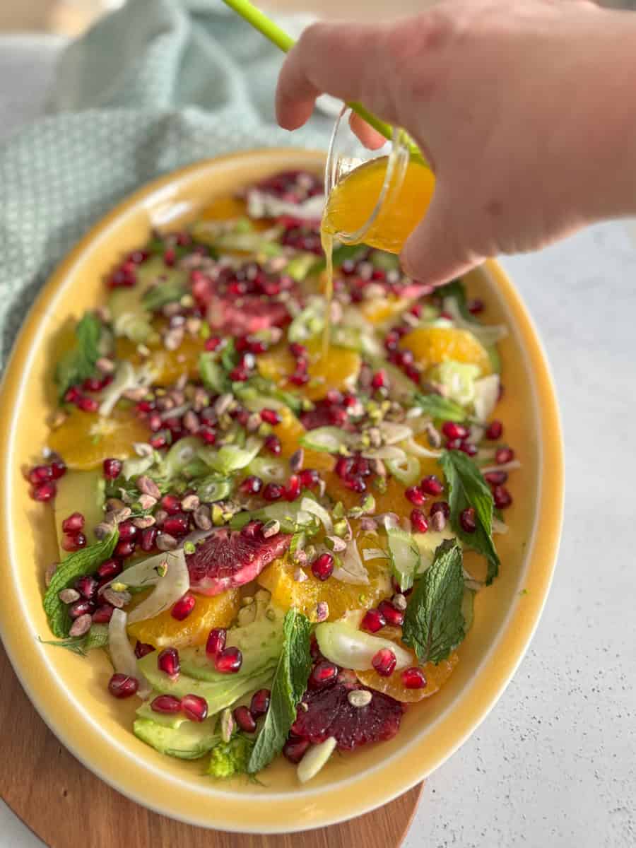 a platter with salad and a hand pouring dressing on top. 