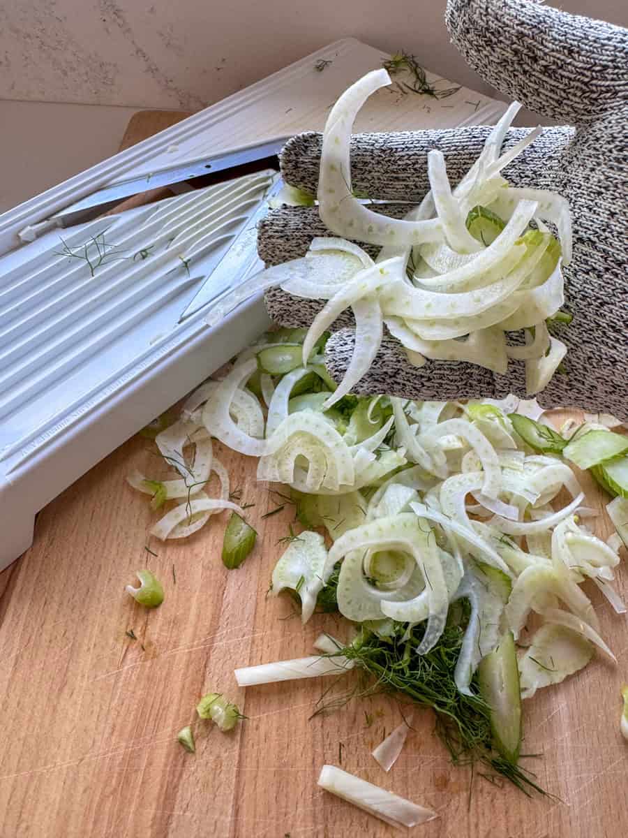 part of mandoline, a hand wearing a safety glove and holding shaved fennel 