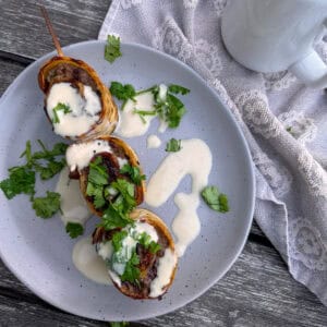 plate with a skewer and 3 beef roll ups with tahini sauce drizzled over it.