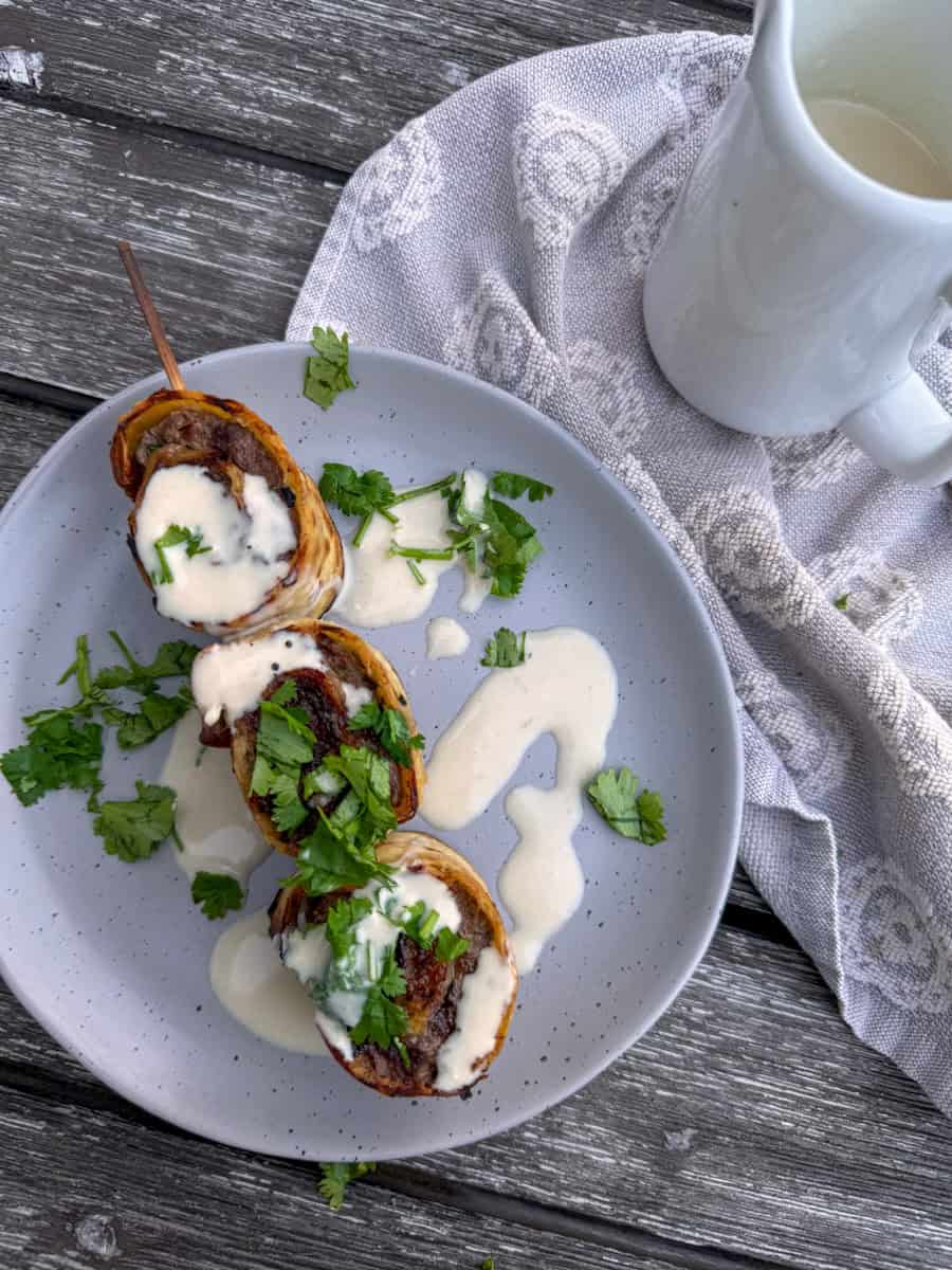 plate with a skewer of rolled up flatbread stuffed with ground beef and drizzled with tahini sauce.