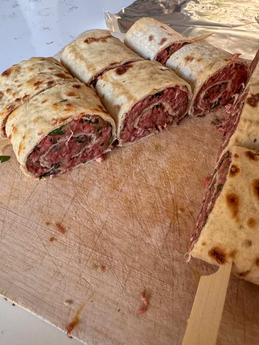 sideview of a skewer with rolls of ground beef wrapped in flatbread 