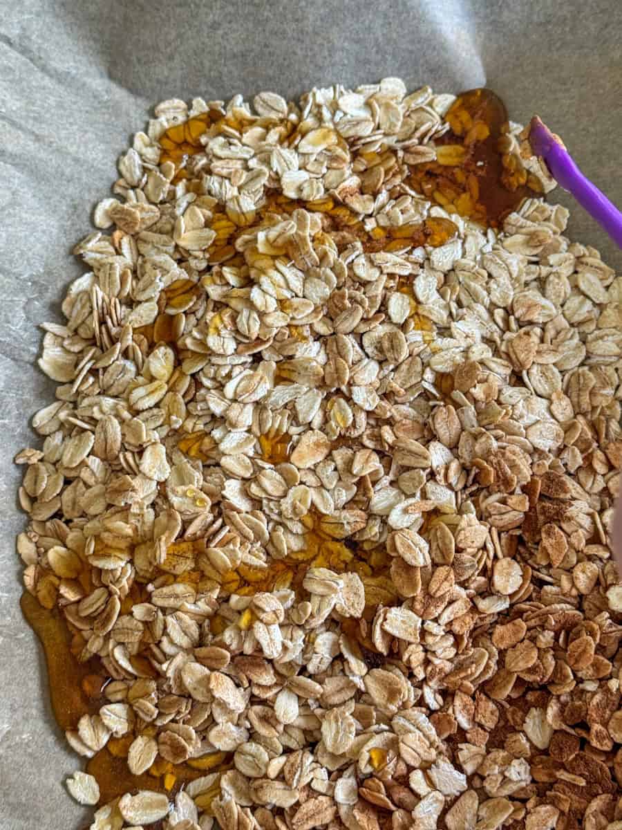 oats spread on baking sheet with maple syrup drizzled 