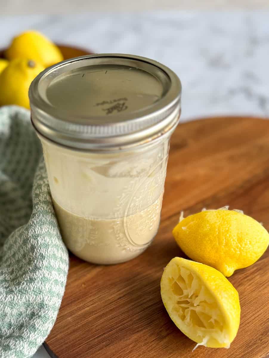 tahini dressing in mason jar with lid and squeezed lemons on side. 