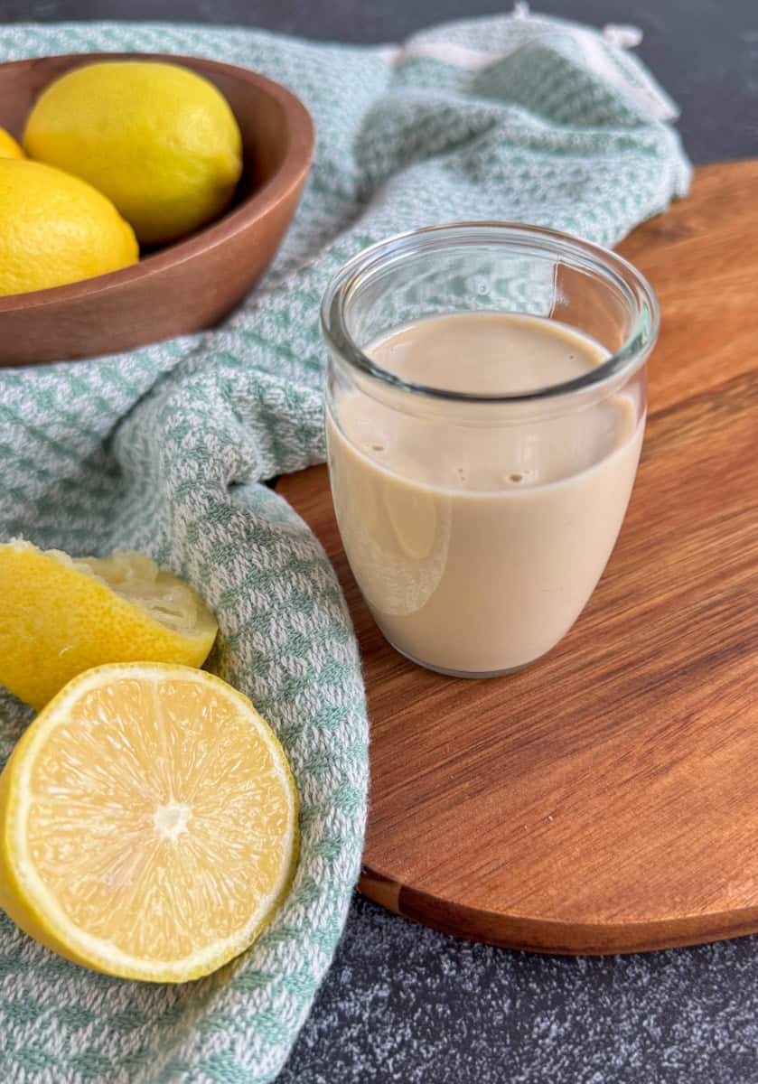 tahini dressing in a small glass jar with lemons on side