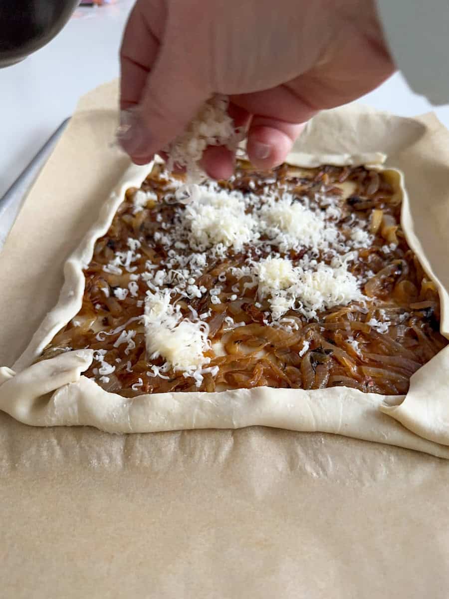 puff pastry tart and a hand sprinkling cheese on top