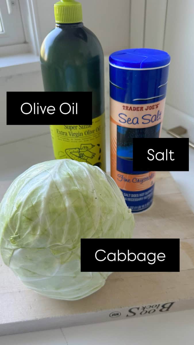 cabbage, salt and olive oil bottle on a cutting board.