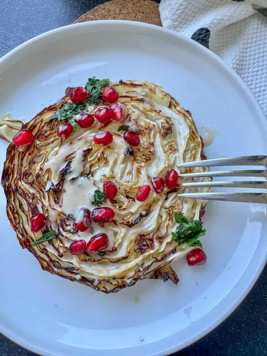 a plate with roasted cabbage piece, fork and sauce and pomegranate seeds