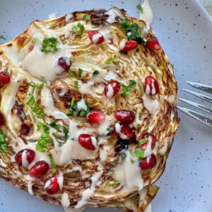 roasted cabbage on a plate drizzled with tahini and pomegranate seeds